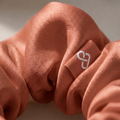 Brown scrunchie with a white logo on a neutral background