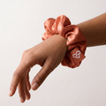 Person wearing a pink scrunchie on wrist with a white heart logo against a light background