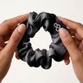 Black scrunchie held between two hands against a white background