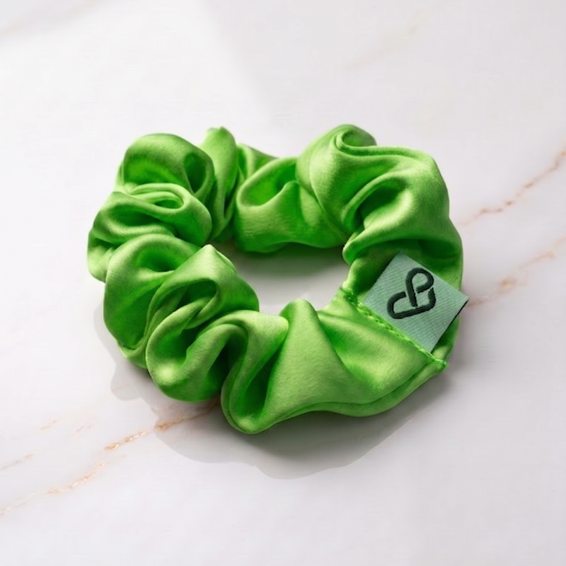 Green scrunchie with a brand tag on a marble surface